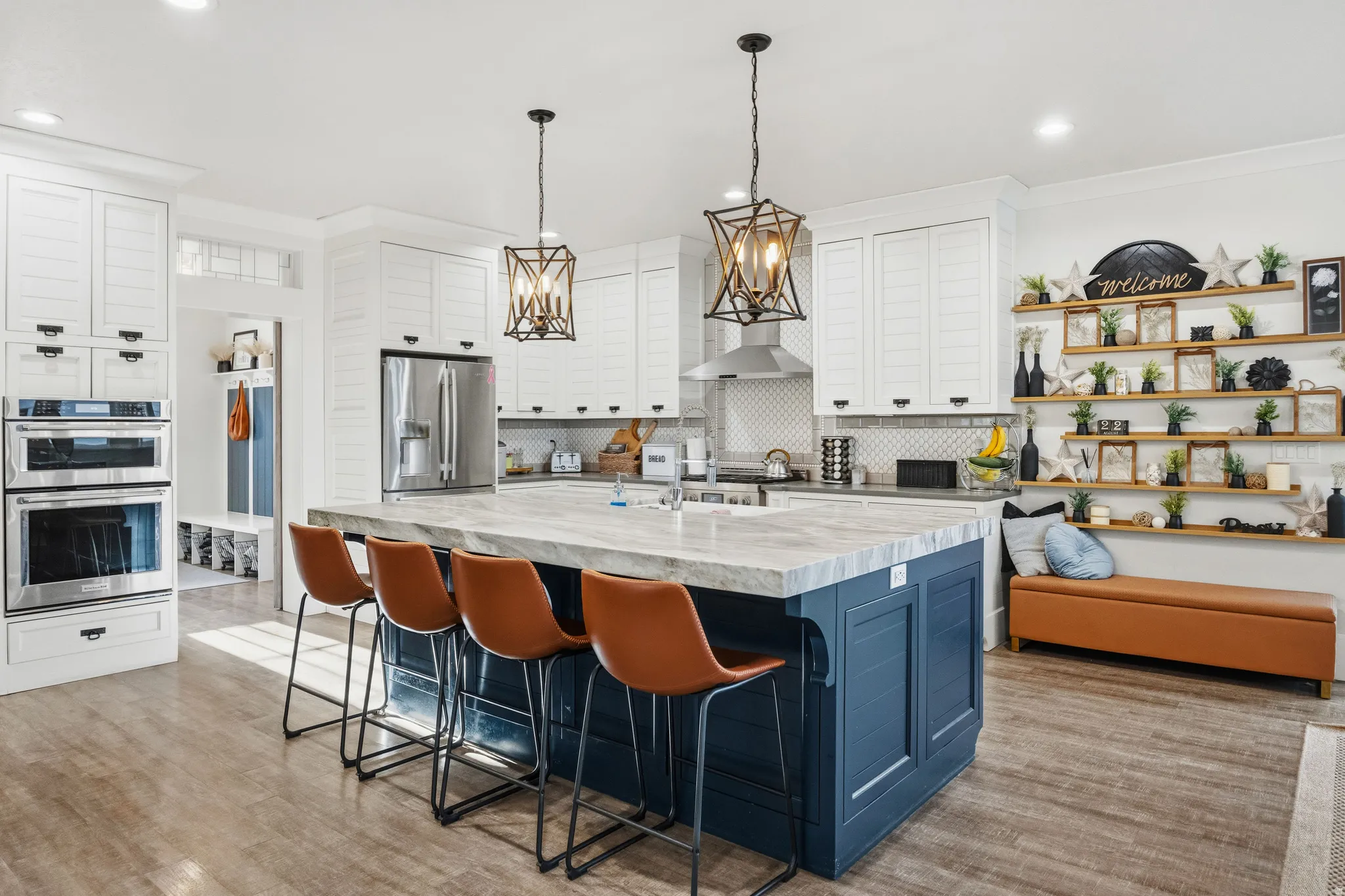 Spacious kitchen featuring an expansive center island, integrated stainless steel appliances, white cabinetry with dark hardware, and wood-finish flooring