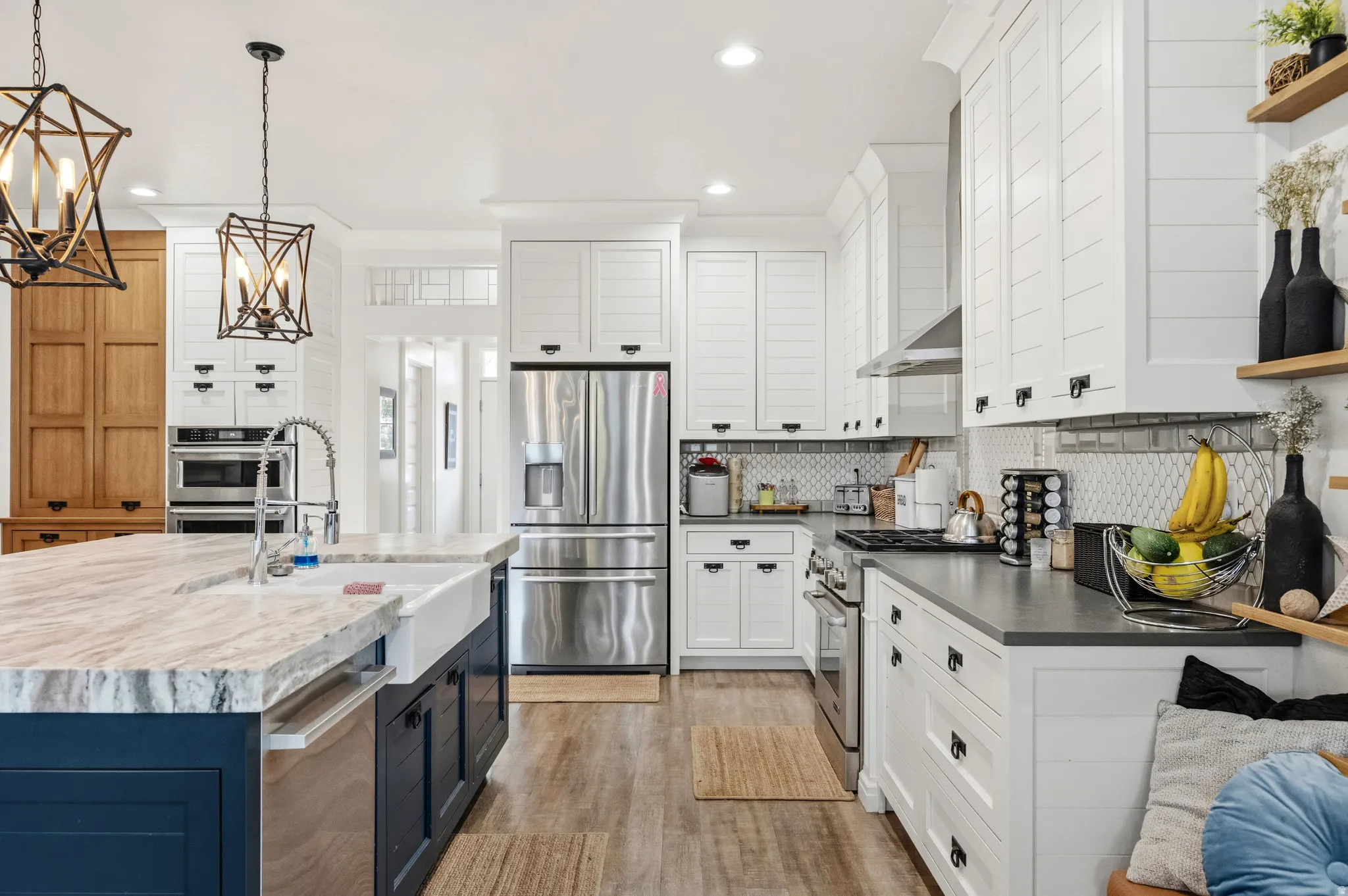 Gourmet kitchen featuring a large island with a farmhouse sink, stainless steel appliances, white shaker-style cabinetry, and wood-finish flooring