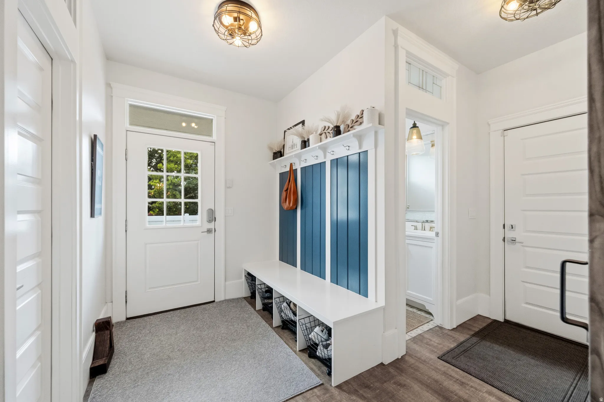 Entryway featuring a built-in bench with hooks, wood-finish flooring, two panel doors, and overhead lighting fixtures