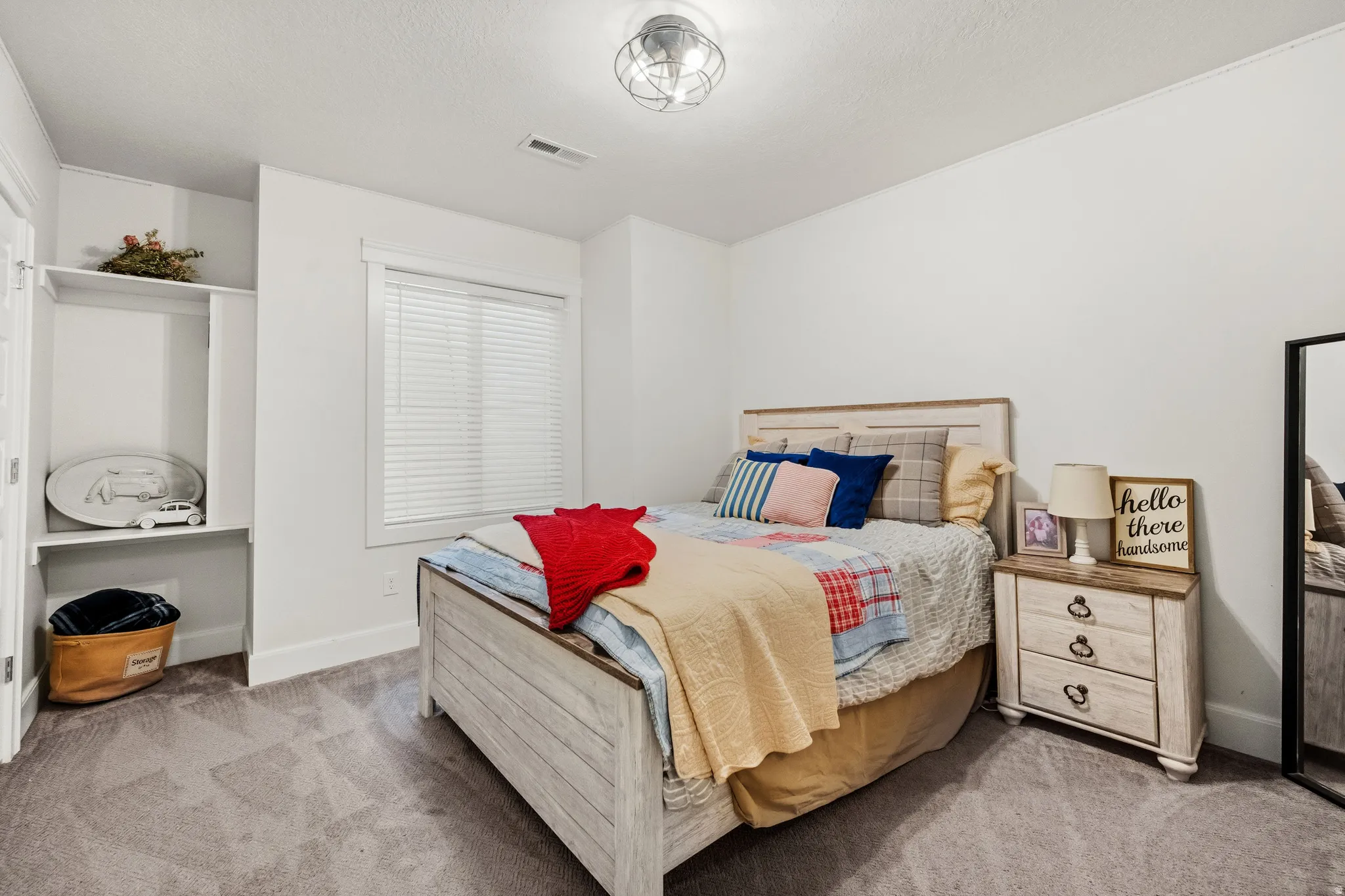 Recessed open shelving, wood-finish bed frame, ceiling-mounted light fixture, window with blinds, and neutral wall paint