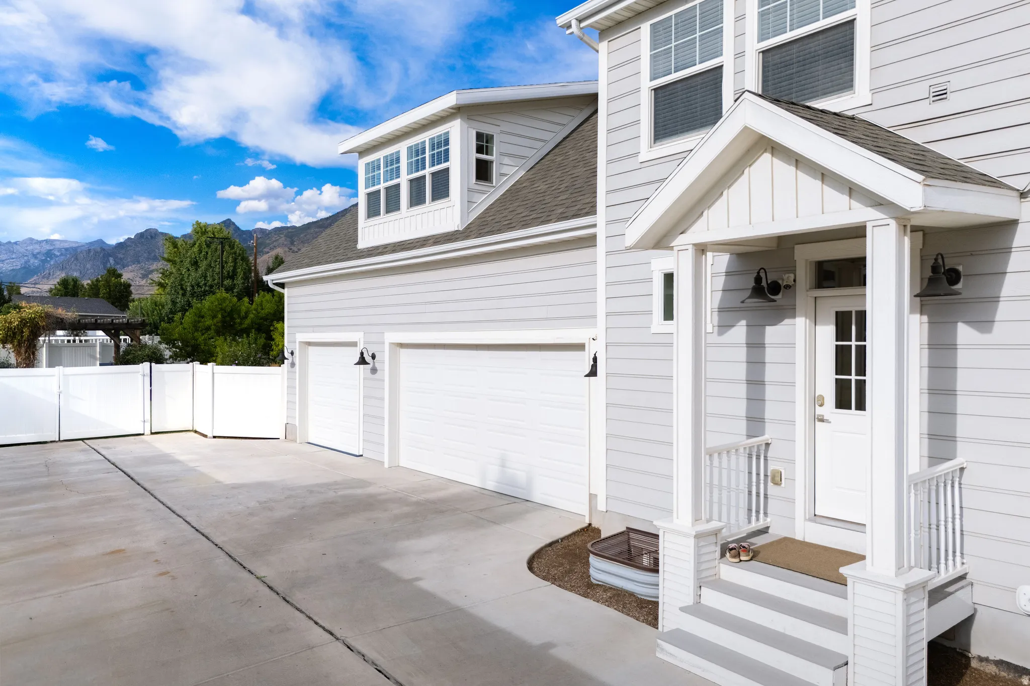 Light gray horizontal siding, covered front entry with white columns, two-car garage, white privacy fence, and concrete driveway