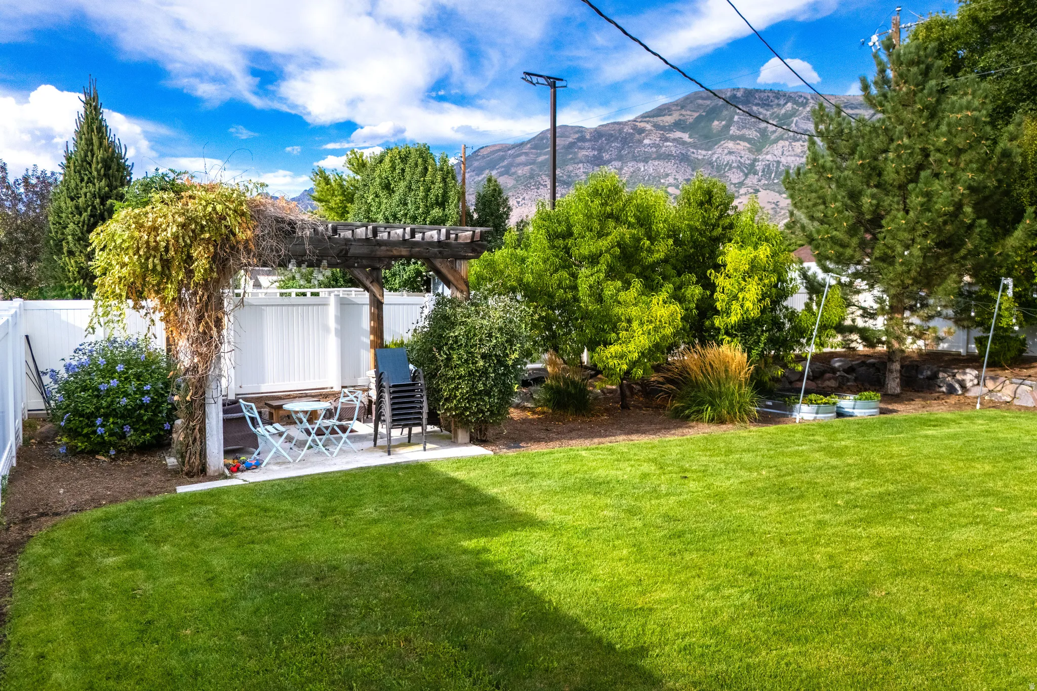 Expansive lawn area with a white privacy fence, an outdoor patio with a wooden pergola, and mature landscaping