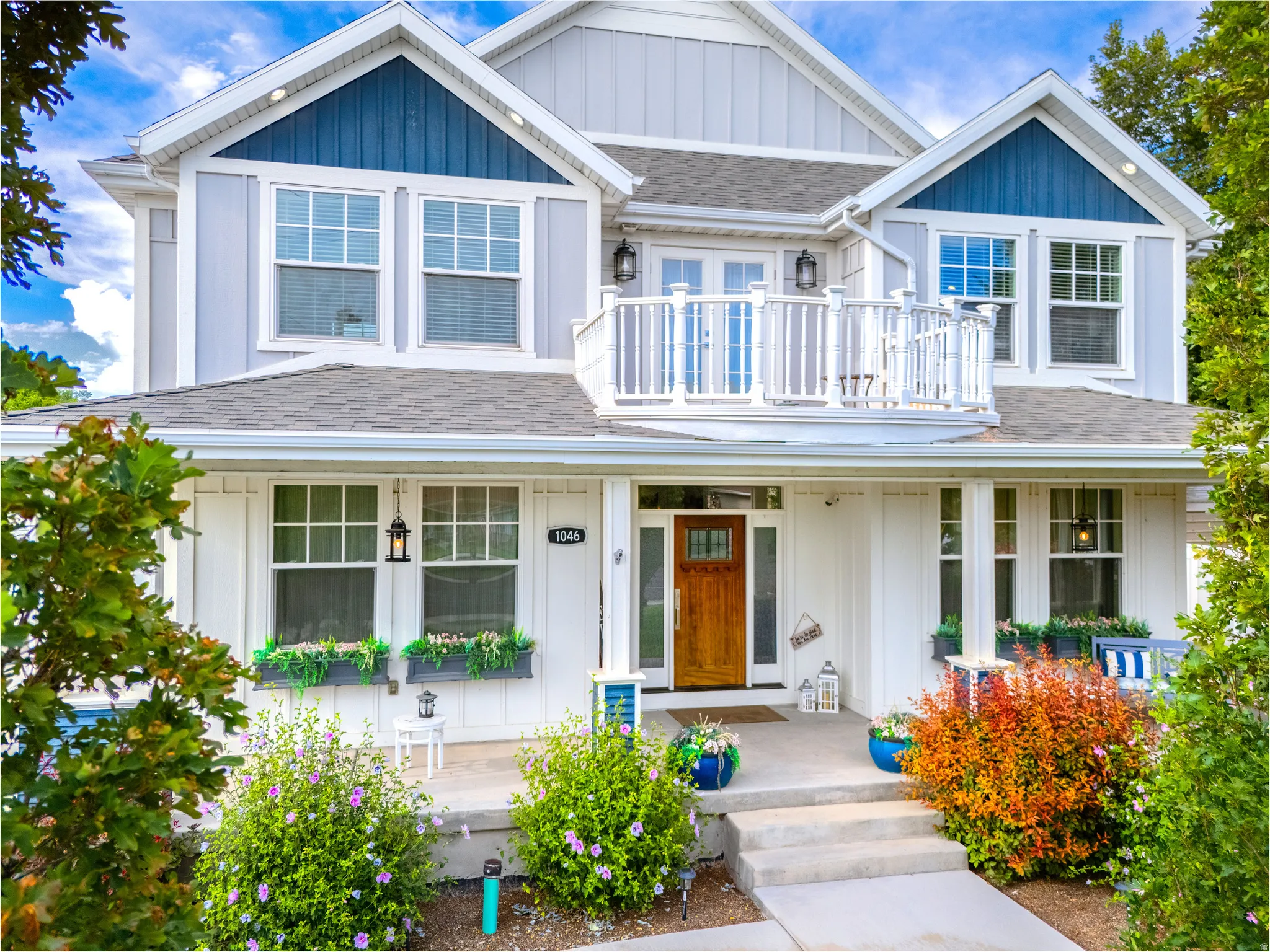 Two-story residence featuring a wood-panel accent gable, an upper-level balcony with white railings, a wood-finish front door, and a concrete porch with steps