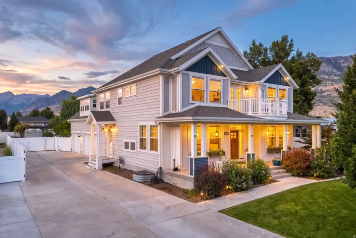 Contemporary home with a covered front porch, white siding, dark trim accents, a second-story balcony, and a multi-car driveway