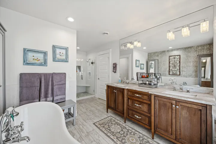 Freestanding bathtub with chrome fixtures, wood-finish flooring, dual vanity with wood cabinetry and undermount sinks, large mirror, and recessed lighting