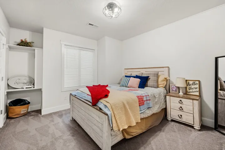 Recessed open shelving, wood-finish bed frame, ceiling-mounted light fixture, window with blinds, and neutral wall paint