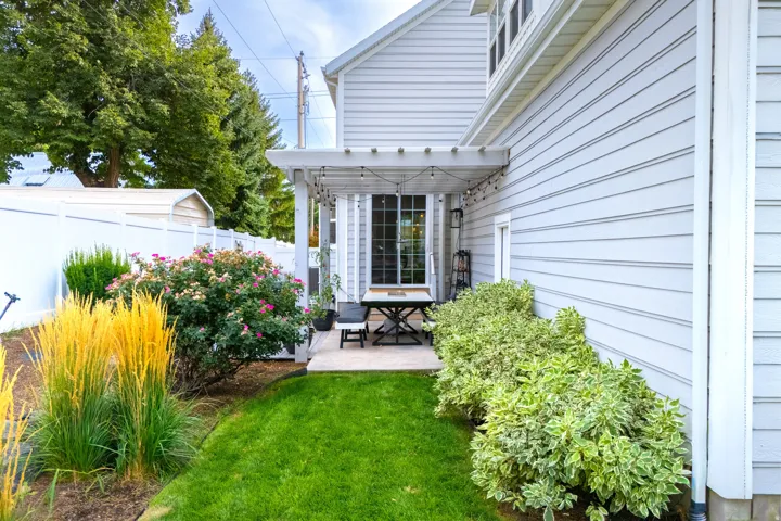 Side yard featuring a concrete patio, white pergola, and extensive landscaping