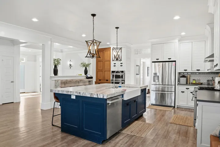 Expansive kitchen featuring a large central island with a farmhouse sink, stainless steel appliances, white perimeter cabinetry, wood-finish flooring, and pendant lighting