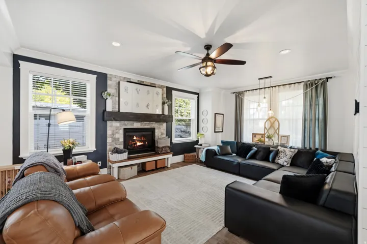 Stone-clad fireplace with a wood-finish mantel, tray ceiling, and a ceiling fan with integrated lighting