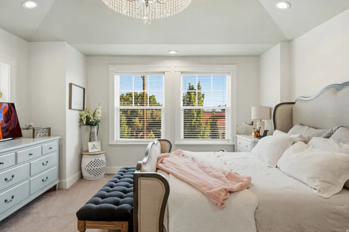 Tray ceiling with recessed lighting, central crystal chandelier, and twin windows