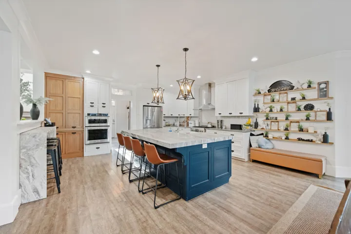 Kitchen featuring a large central island with seating, pendant lighting, built-in double ovens, and wood-finish flooring