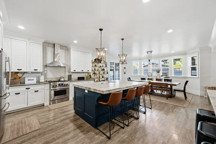 Open-concept kitchen with a substantial island, wood-finish flooring, white cabinetry, stainless steel appliances, and a dining area with multiple windows