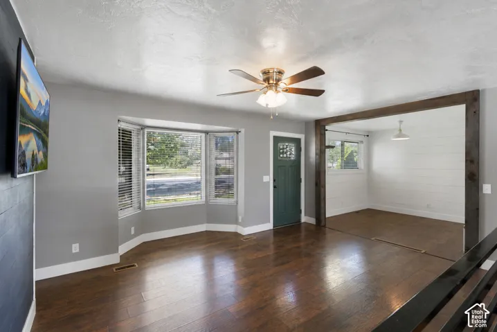 Rich wood-finish flooring, a bay window with natural light, and a ceiling fan with integrated lighting
