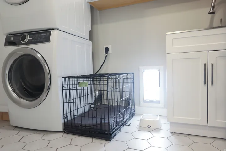 White hexagon tile flooring, stacked laundry appliances, white cabinetry with silver hardware, and a built-in pet door