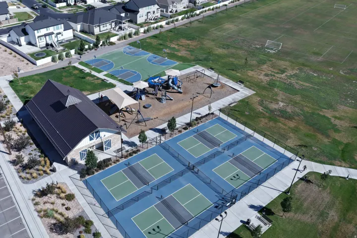 Four pickleball courts, two basketball courts, a playground area, a community building with a metal roof, and an expansive sports field