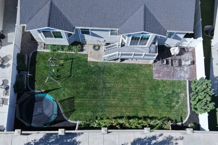 Expansive green lawn with a white privacy fence, a multi-level deck, and a paved patio area