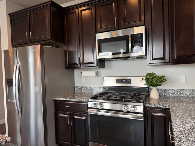 Dark wood-finish cabinetry with silver-tone hardware, granite countertops, stainless steel gas range, stainless steel microwave, and stainless steel refrigerator