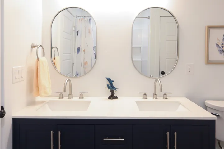 Dual undermount sinks with brushed nickel faucets, white countertop, and dark blue vanity cabinetry
