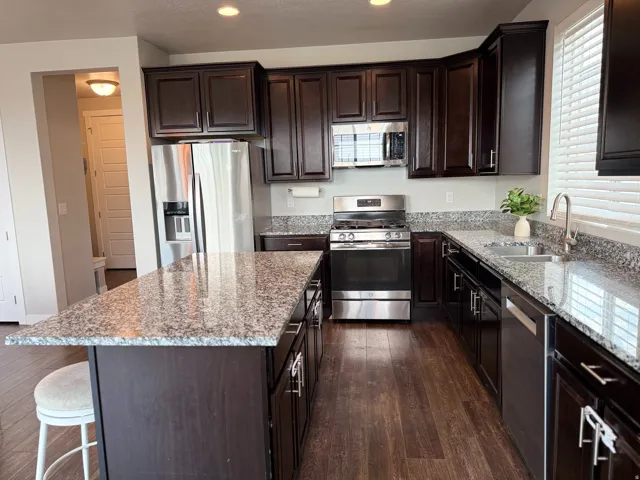 Dark wood-finish cabinetry, stainless steel appliances, granite countertops, wood-finish flooring, and a large kitchen island