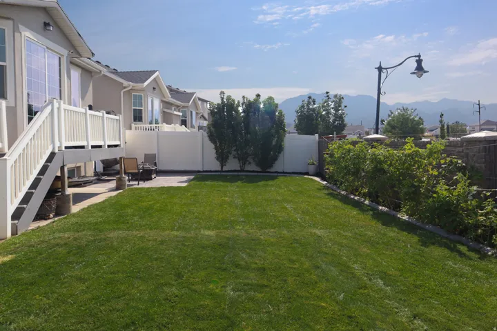 Expansive lawn area with a paved patio, a white privacy fence, and mature landscaping