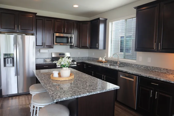 Dark wood cabinetry with brushed nickel hardware, stainless steel appliances, speckled stone countertops, a kitchen island with seating, and wood-finish flooring