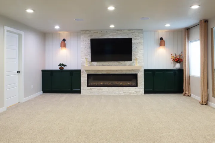 Built-in entertainment wall with electric fireplace, stone surround, wood mantel, and integrated dark green cabinetry