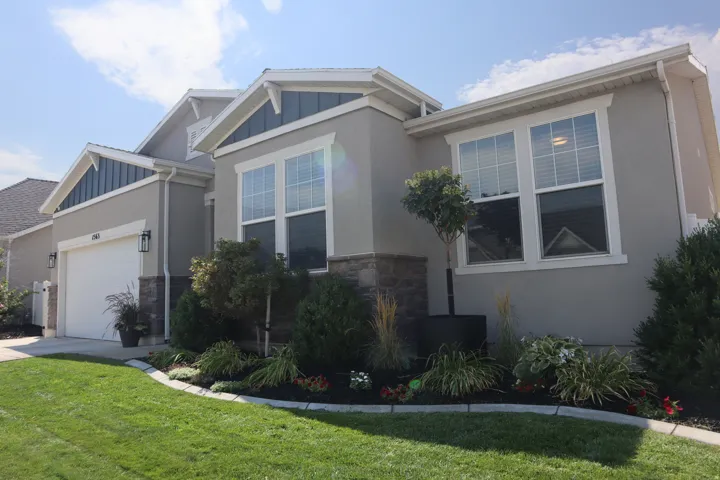 Stucco exterior with stone accents, integrated garage, white trim windows, and landscaped front yard with decorative plantings