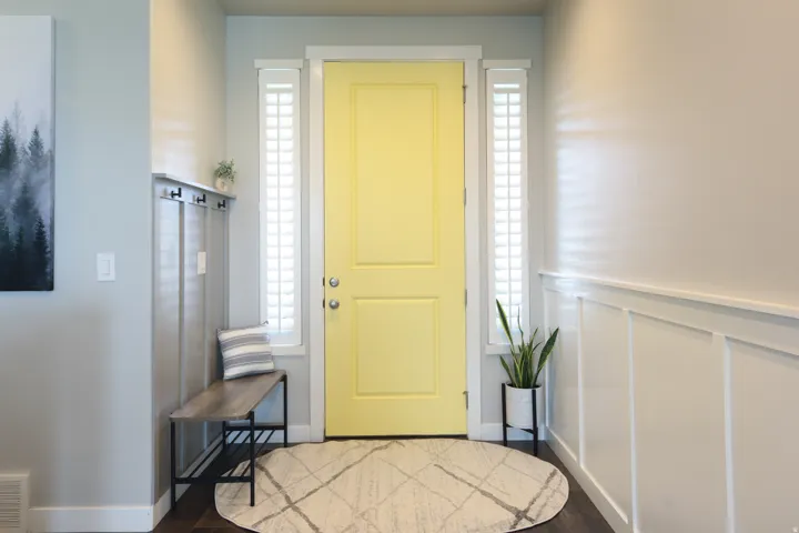 Entryway featuring a bright yellow door with sidelight windows, dark wood-finish flooring, and white wainscoting