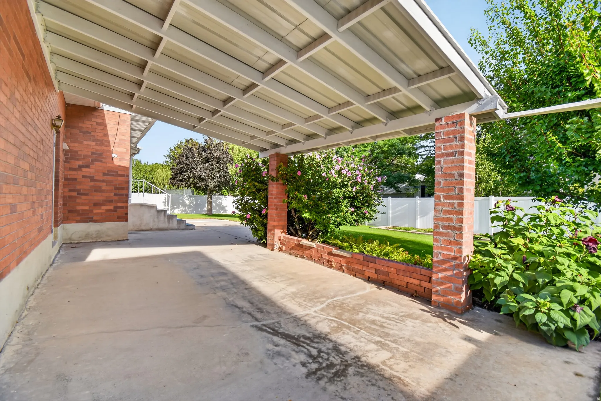 Covered patio area with concrete flooring, brick columns, and an adjacent landscaped garden bed