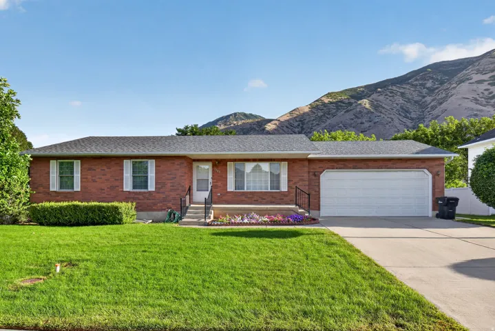 Brick exterior, attached two-car garage, concrete driveway, mature landscaping, and mountain backdrop