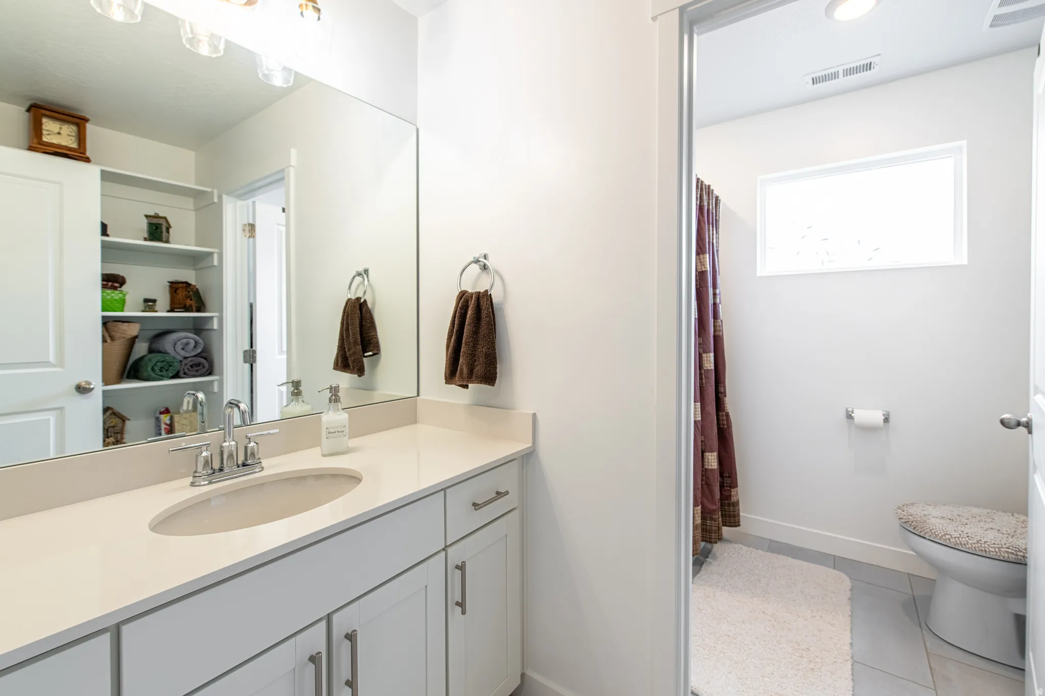 Bathroom featuring a white vanity with an undermount sink, a light-toned countertop, and recessed shelving