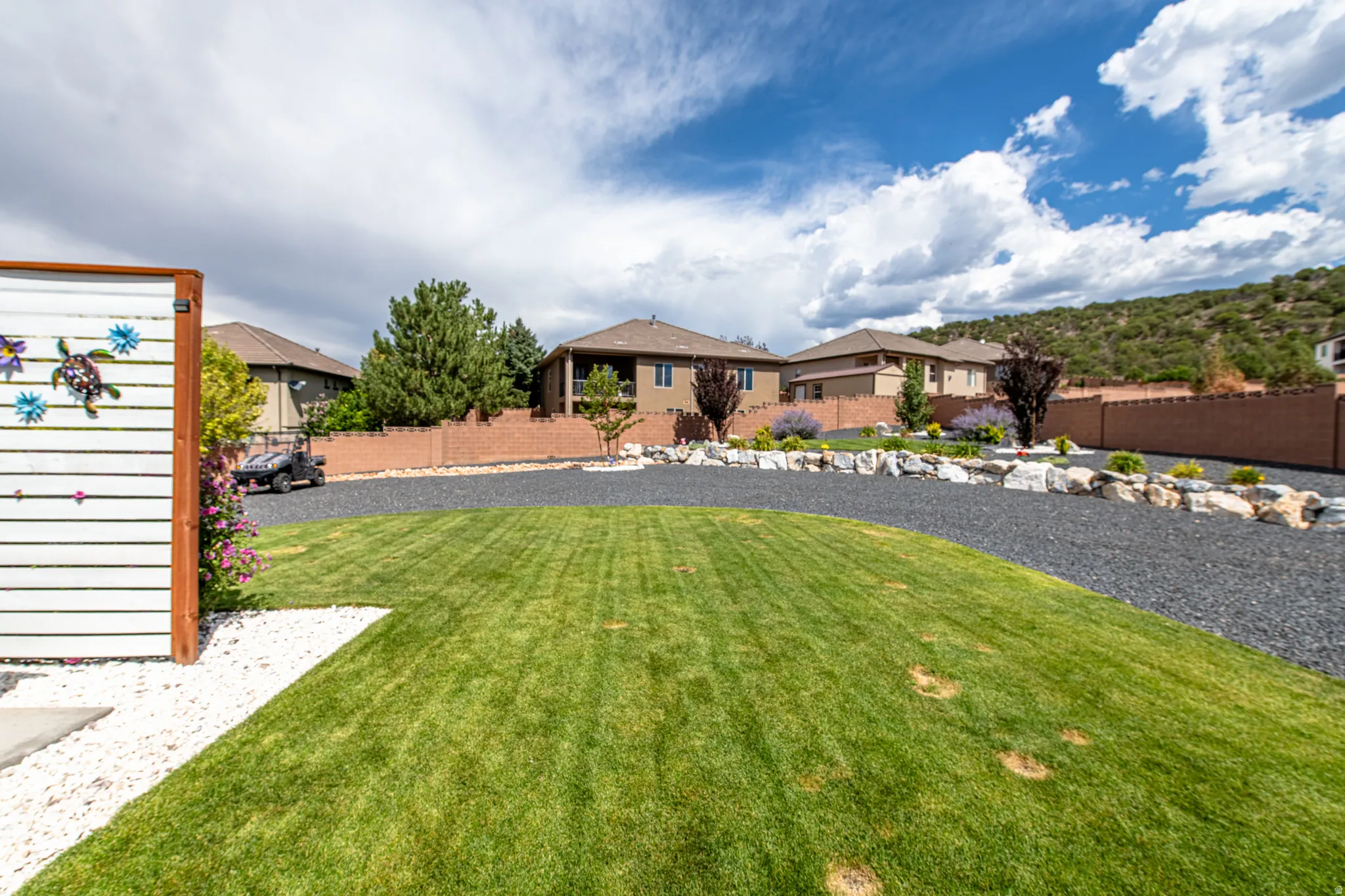 Expansive lawn area with white gravel accent, dark gravel driveway, stone retaining walls, and mature landscaping