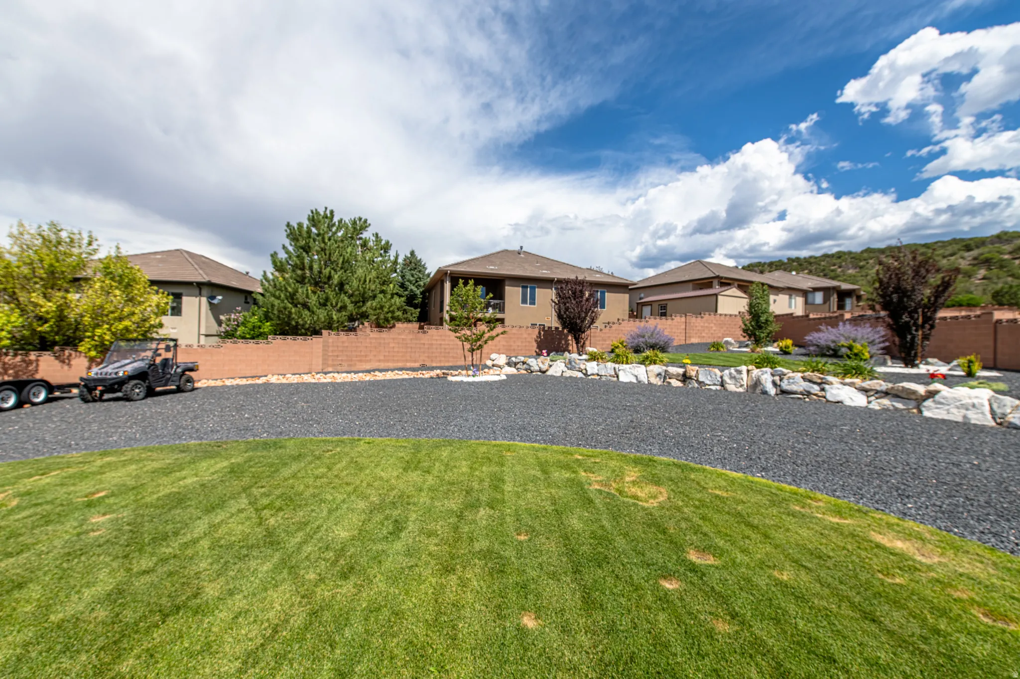 Expansive exterior featuring a manicured lawn, dark aggregate driveway, and a stone retaining wall