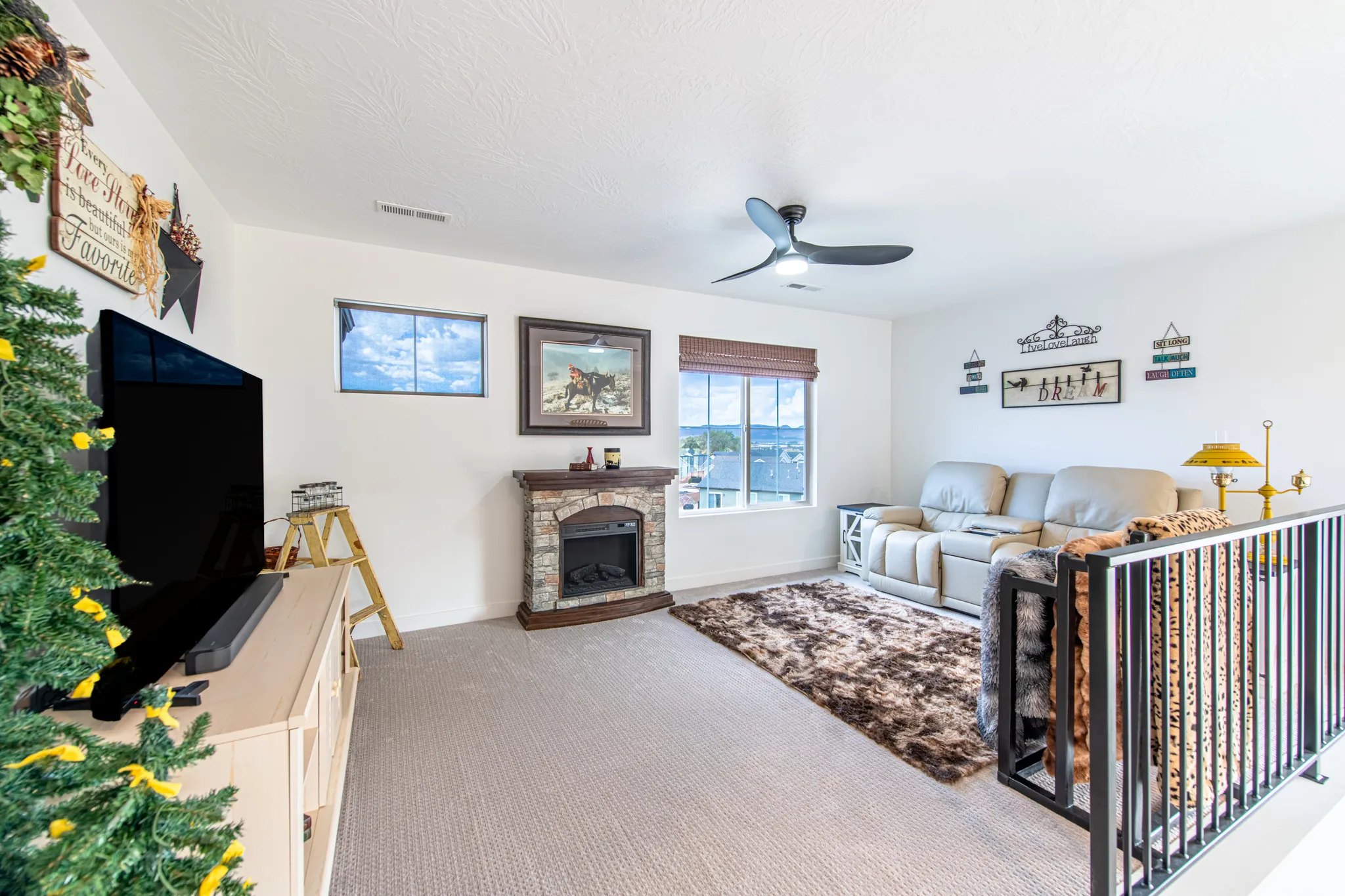 Carpeted living area featuring a stone-faced fireplace, two distinct windows, and a ceiling fan