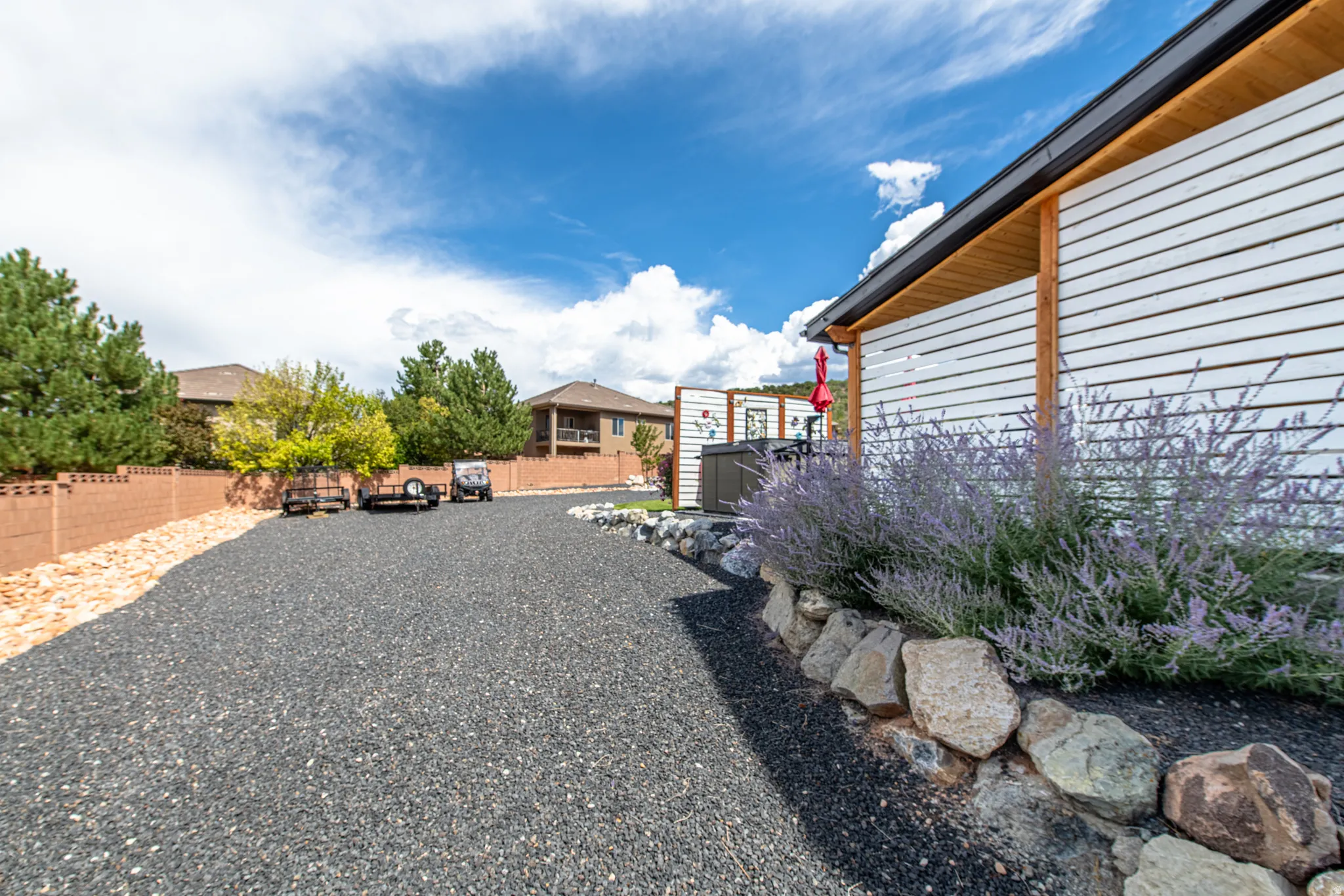Gravel drive, white horizontal siding, wood-finish soffit, dark gutters, rock border landscaping