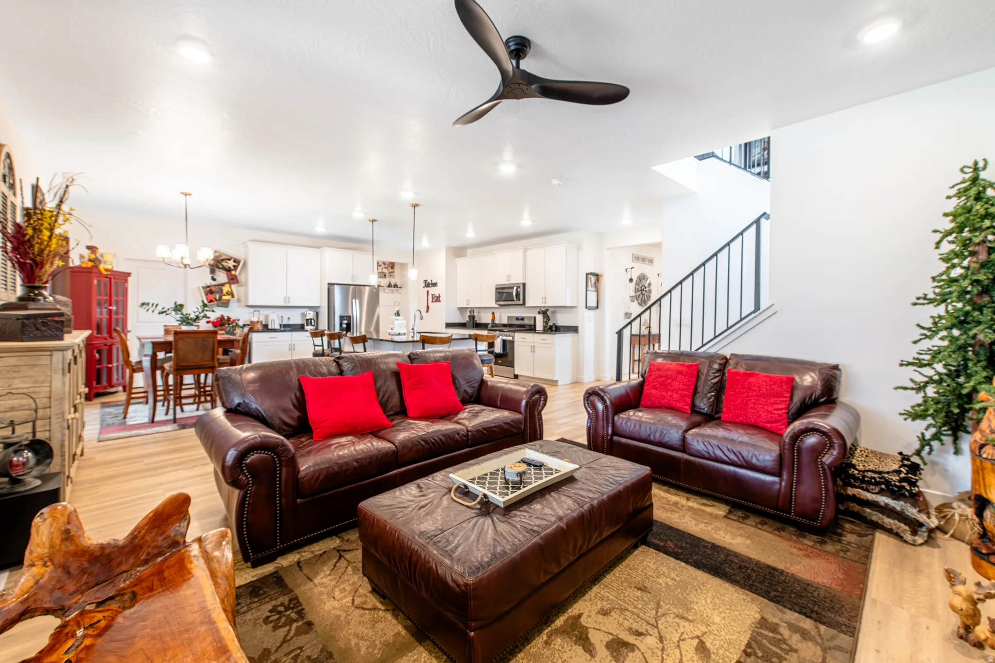 Open-concept living area featuring wood-finish flooring, a contemporary ceiling fan, recessed lighting, and a kitchen with white cabinetry and stainless steel appliances