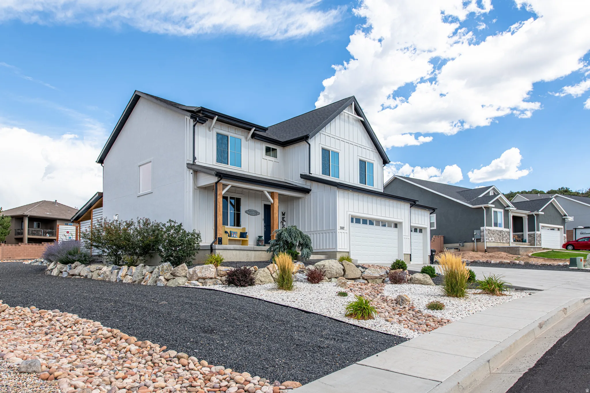 Modern farmhouse-style exterior with a two-car garage, covered entry porch with wood columns, and a landscaped front yard featuring decorative rock and plantings
