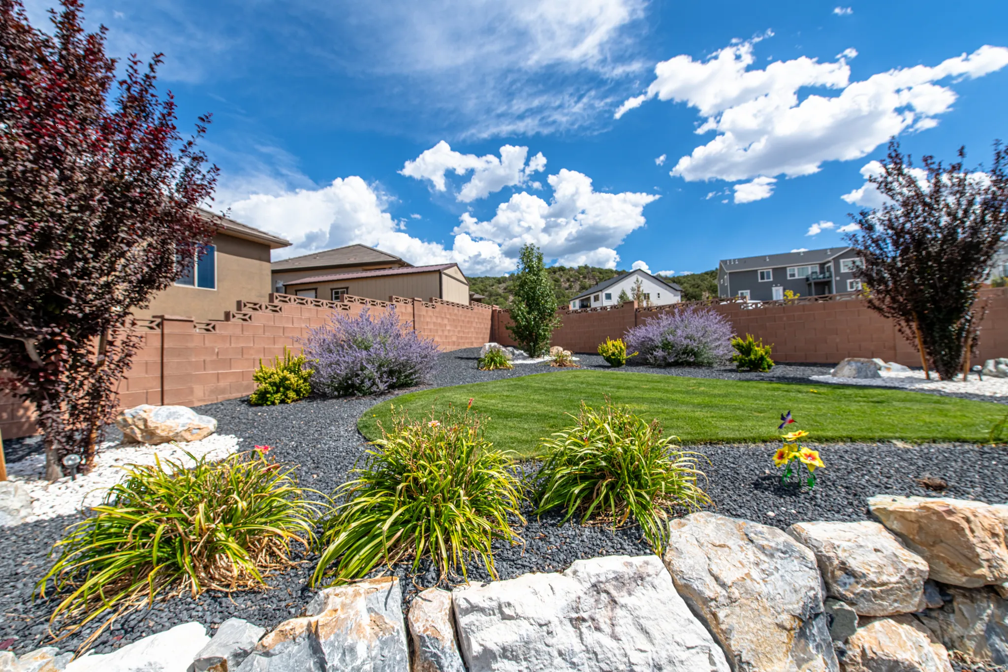 Landscaped backyard featuring a manicured lawn, established shrubs, and decorative rock beds