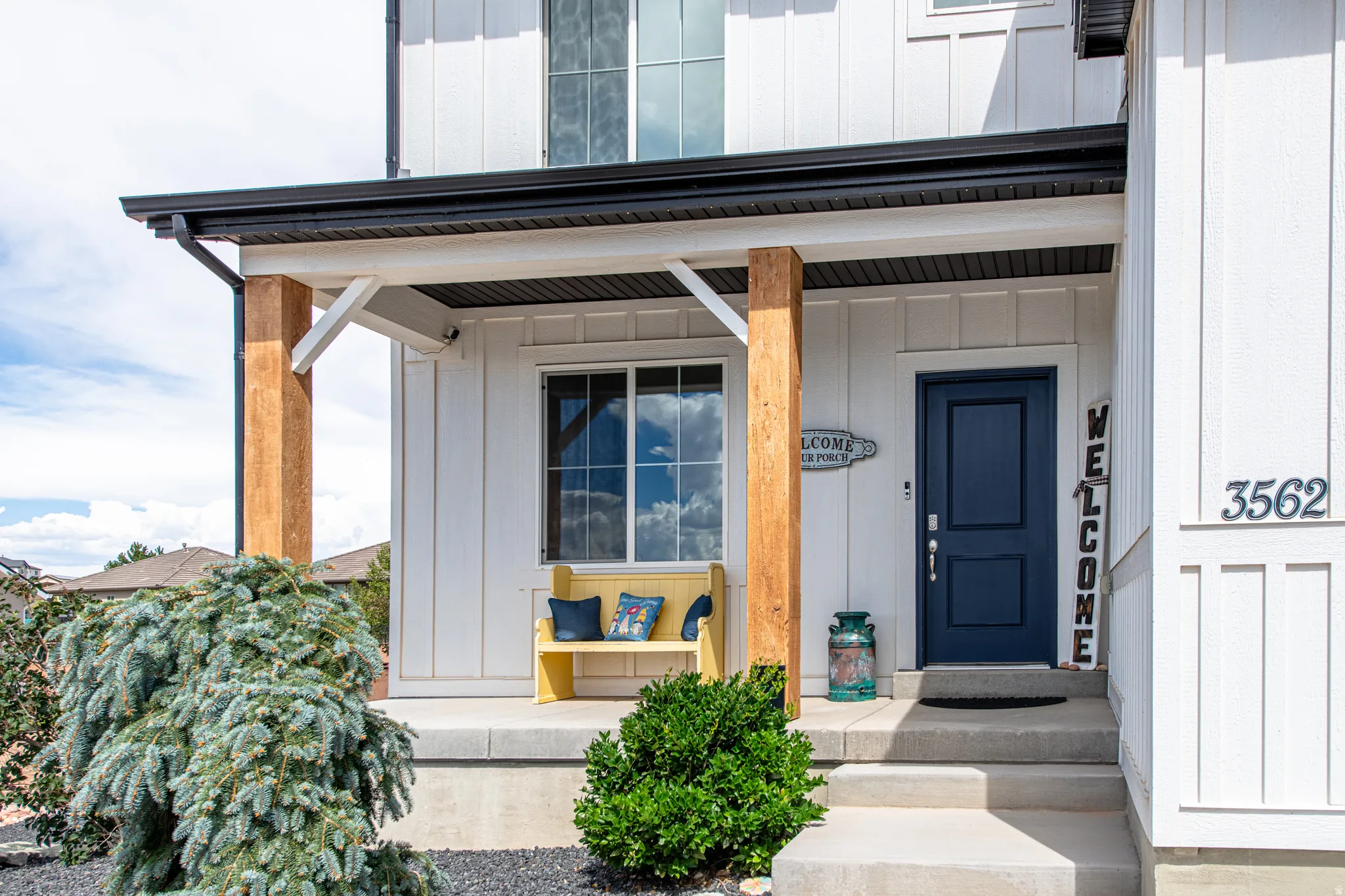 Board and batten exterior with a covered entry, wood-finish support columns, a dark-toned entry door, and concrete steps