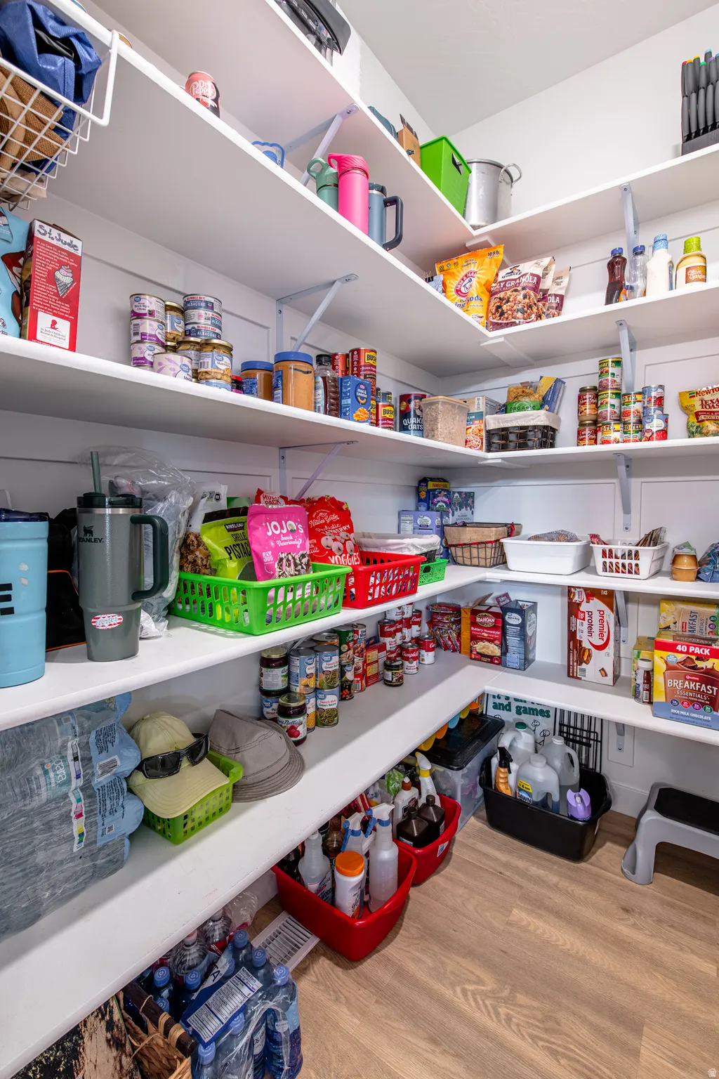 Walk-in pantry featuring white shelving, wood-finish flooring, and ample storage