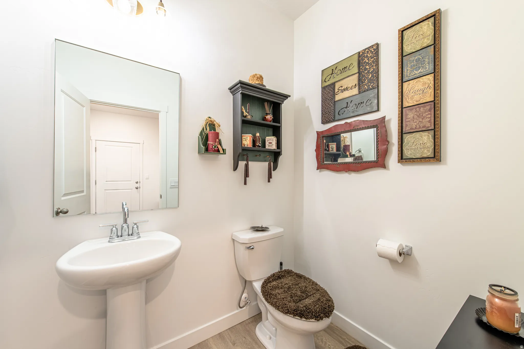 Pedestal sink with chrome fixtures, wall-mounted mirror, light wood-finish flooring, and a white toilet