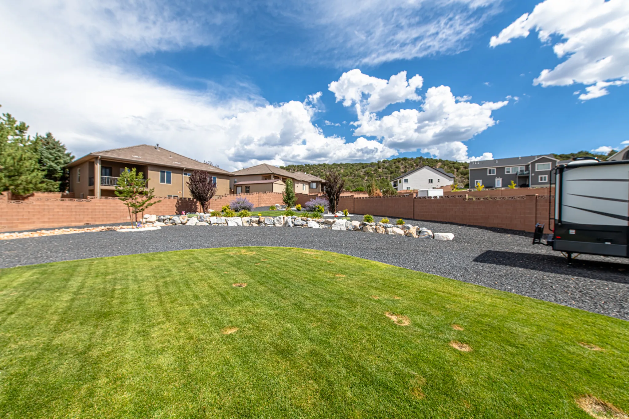 Expansive outdoor area featuring a manicured lawn, a gravel drive, and a retaining wall