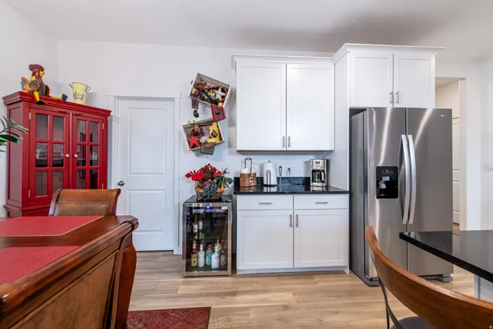 Stainless steel refrigerator, white shaker-style cabinetry, black countertops, wood-finish flooring, and a built-in beverage cooler
