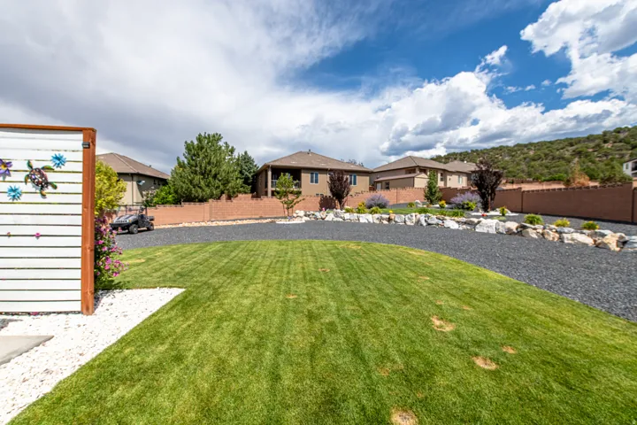 Expansive lawn area with white gravel accent, dark gravel driveway, stone retaining walls, and mature landscaping