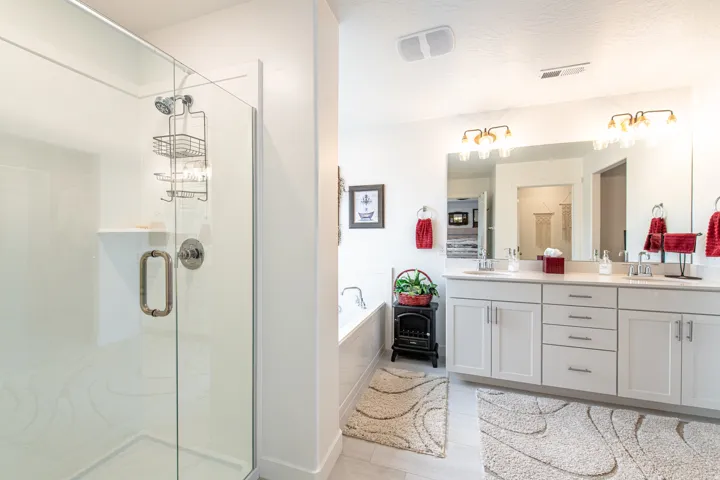 Glass-enclosed shower with a built-in shelf, dual vanity with a large mirror, light-toned cabinetry, and a built-in soaking tub