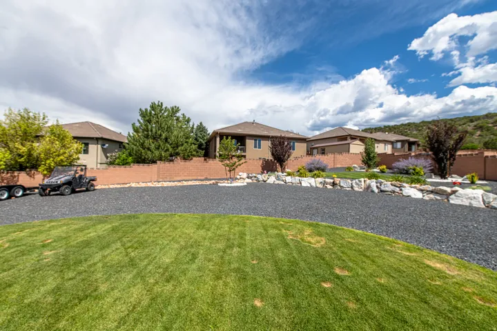Expansive exterior featuring a manicured lawn, dark aggregate driveway, and a stone retaining wall