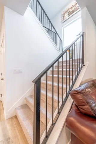 Carpeted staircase with black metal balusters and handrail, featuring wood-finish flooring at the base