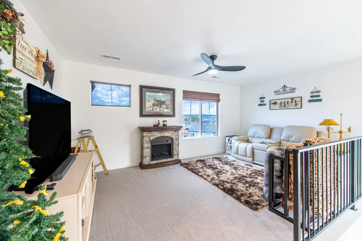 Carpeted living area featuring a stone-faced fireplace, two distinct windows, and a ceiling fan