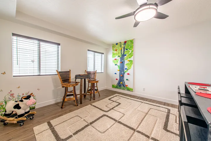 Wood-finish flooring with white baseboards, two windows with blinds, and an overhead ceiling fan with integrated lighting