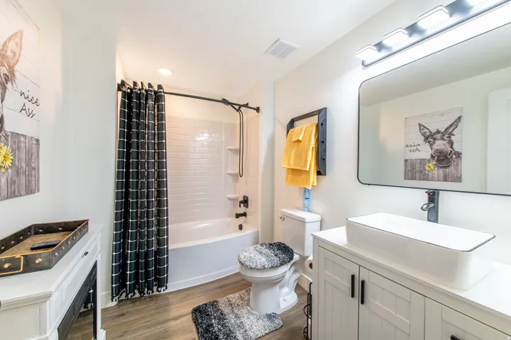 White subway tile shower surround with a built-in niche, vessel sink, vanity with shaker-style doors, and wood-finish flooring